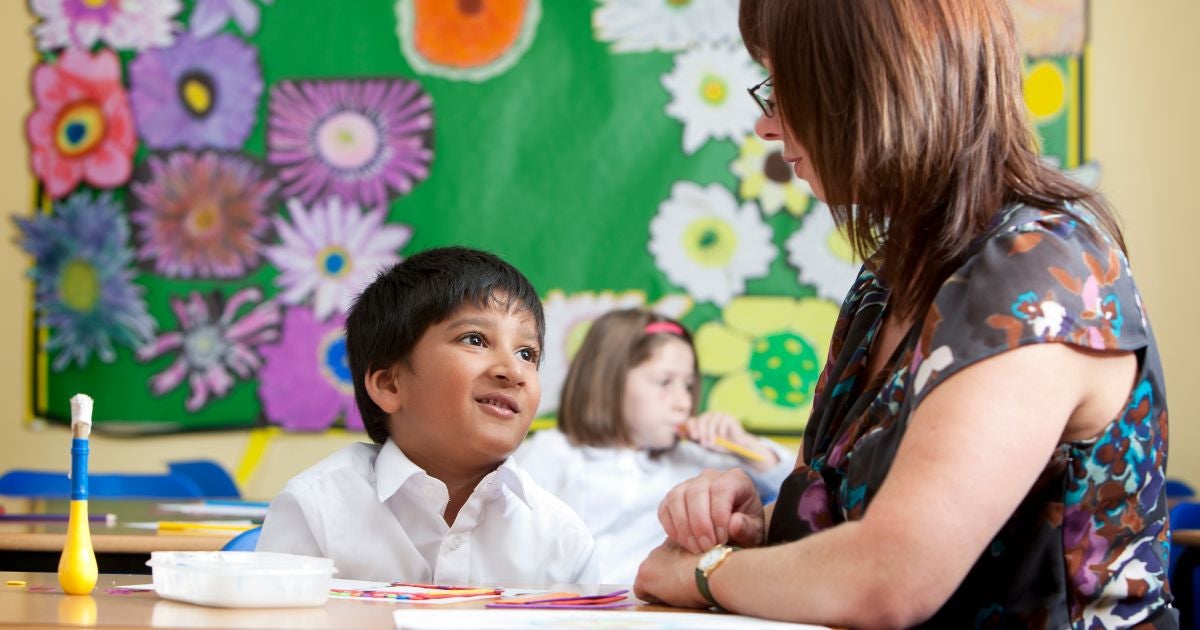 Primary school student sitting with his teacher doing work